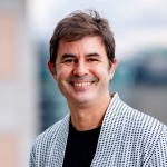 portrait of a man with short dark hair, wearing a black T-shirt and gray blazer