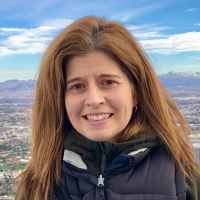 woman with long, brown hair, wearing black puffer jacket smiles at camera