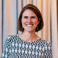 Smiling woman with short, dark hair, wearing a black and white print dress. 