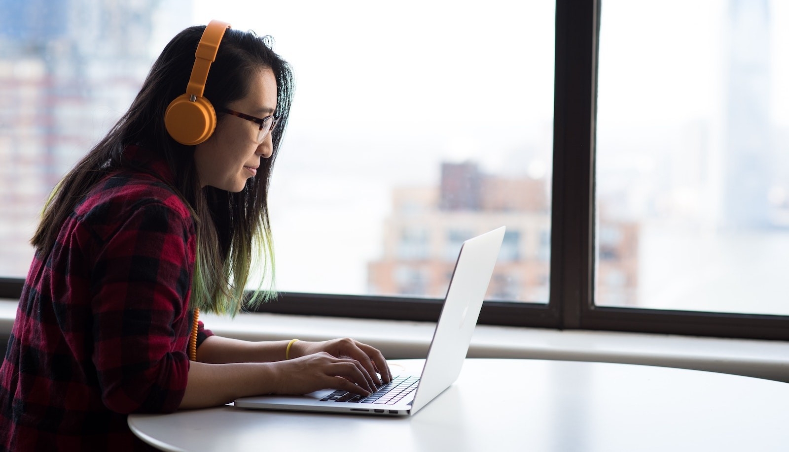 A person is looking at a laptop, wearing orange headphones.