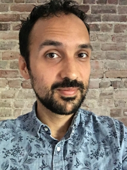 Thomas Khullar wears a blue shirt in front of a brick wall