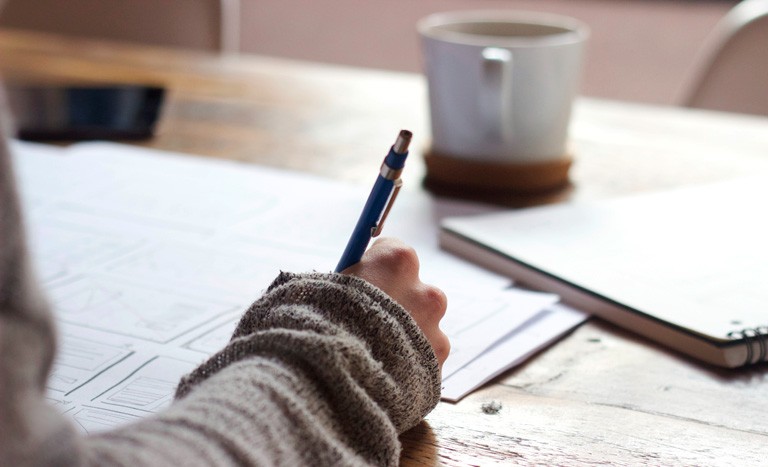 Person taking notes with a cup of tea