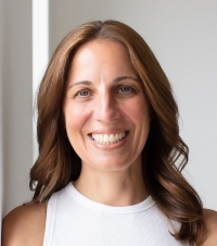 Smiling woman with brown hair in a white top looking straight ahead
