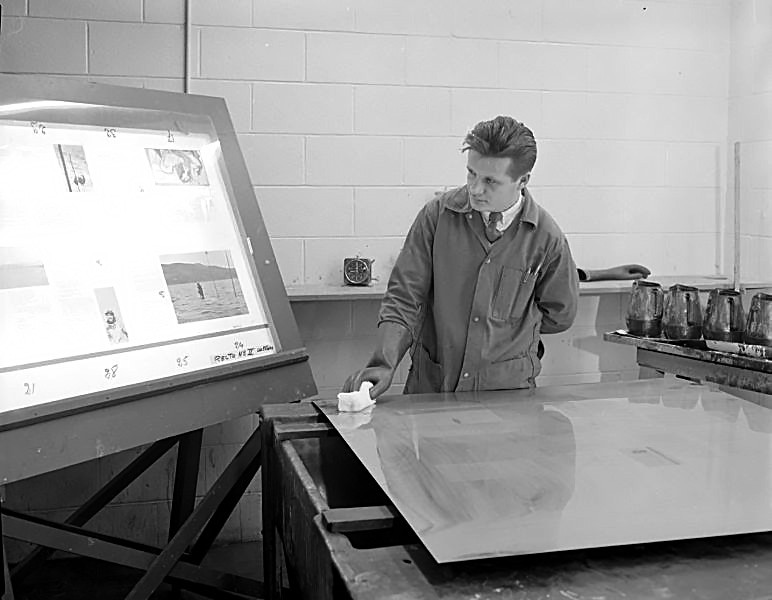A man prepares a printing plate while looking at a sample board.