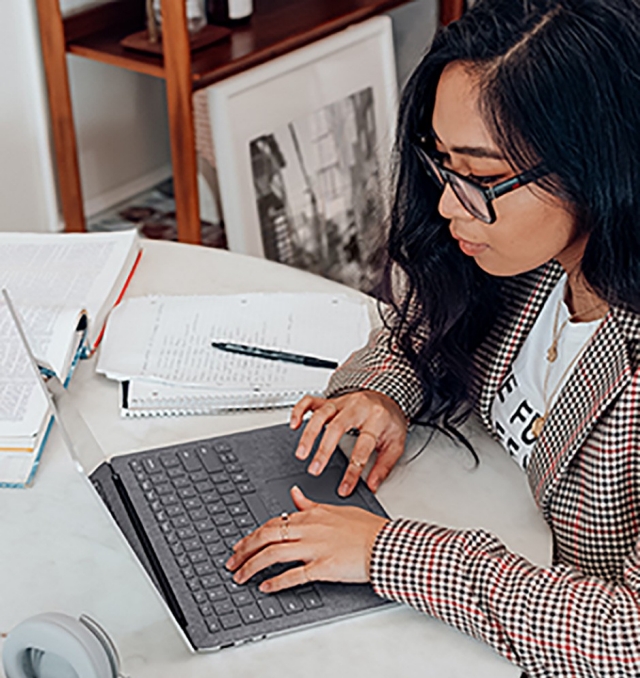 woman sitting studying at a desk with a laptop, notebook and textbook