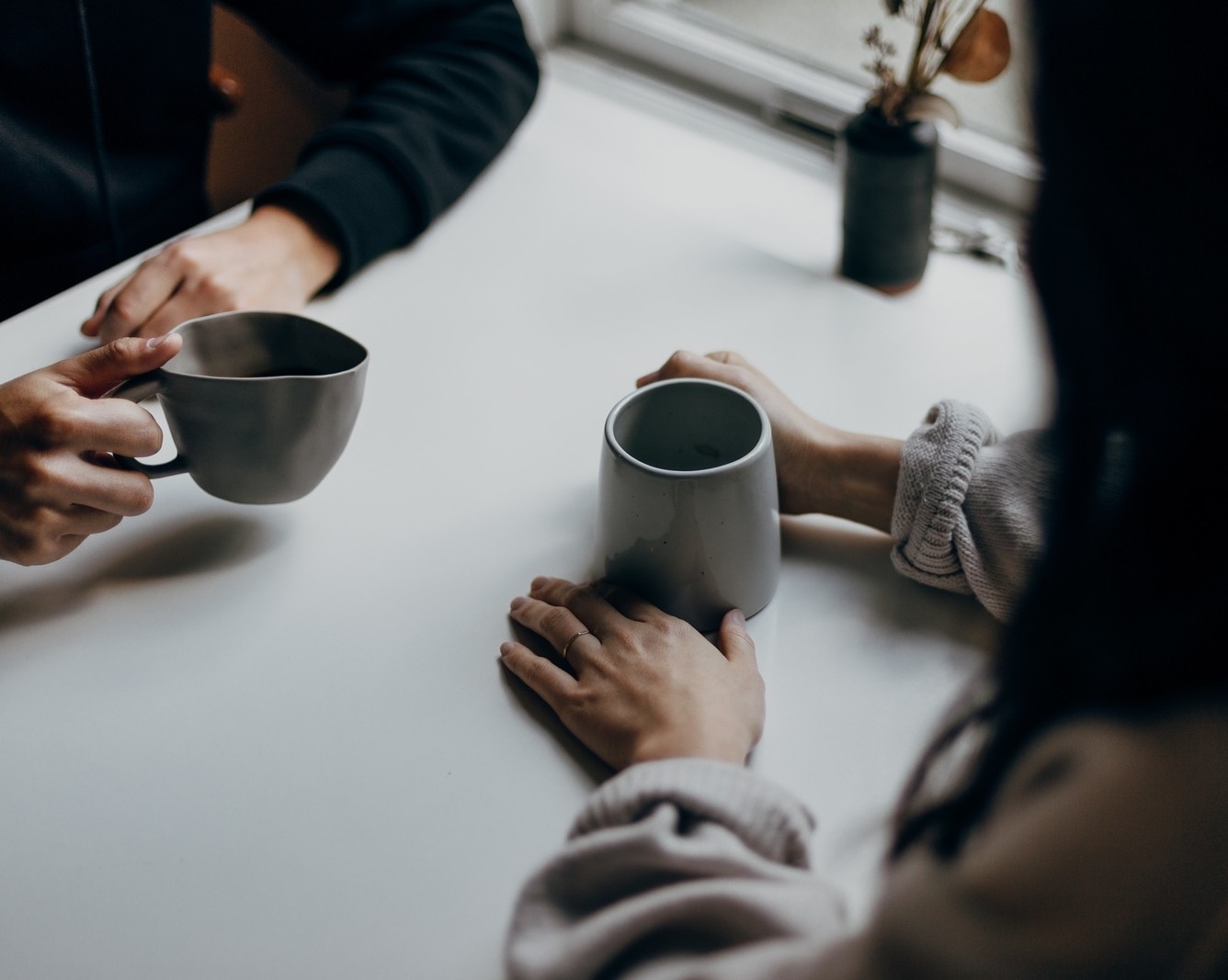 Two people's hands holding coffee mugs at a table