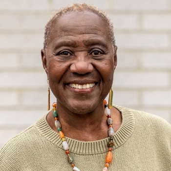 headshot of smiling woman with short hair, wearing a light-green sweater and colourful beaded necklace