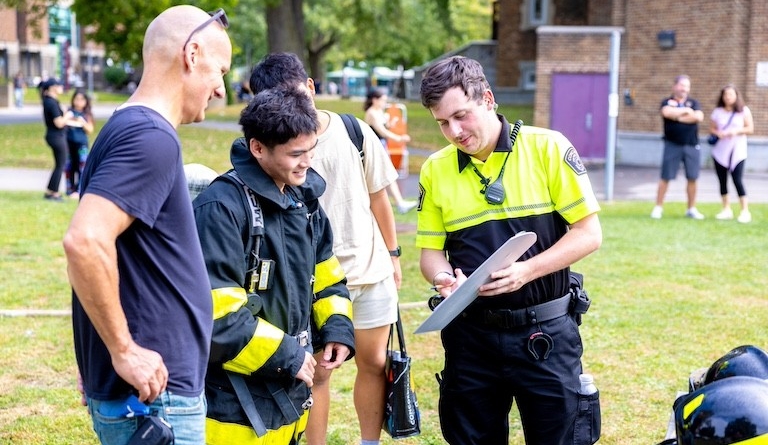 A man wearing a reflective security shirt explaining something to two other men.