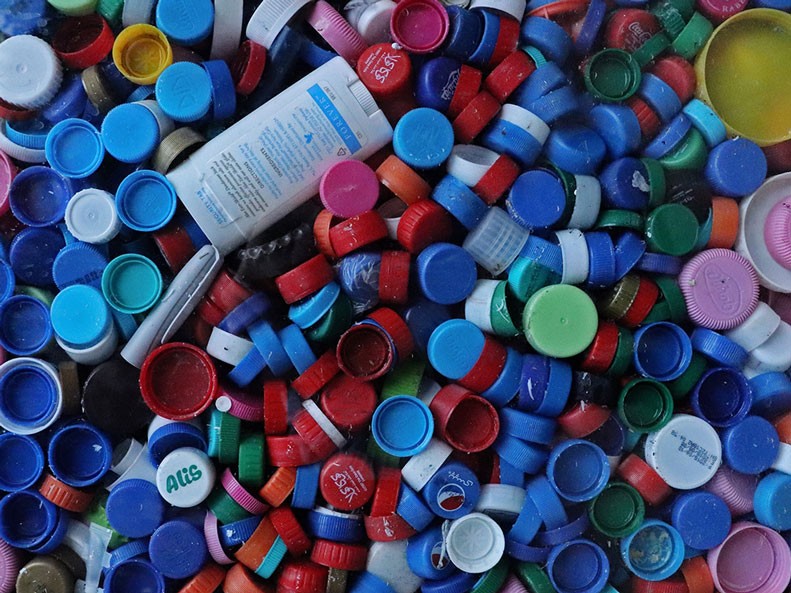 A set of four collection bins of different colours sit on the sidewalk against a building