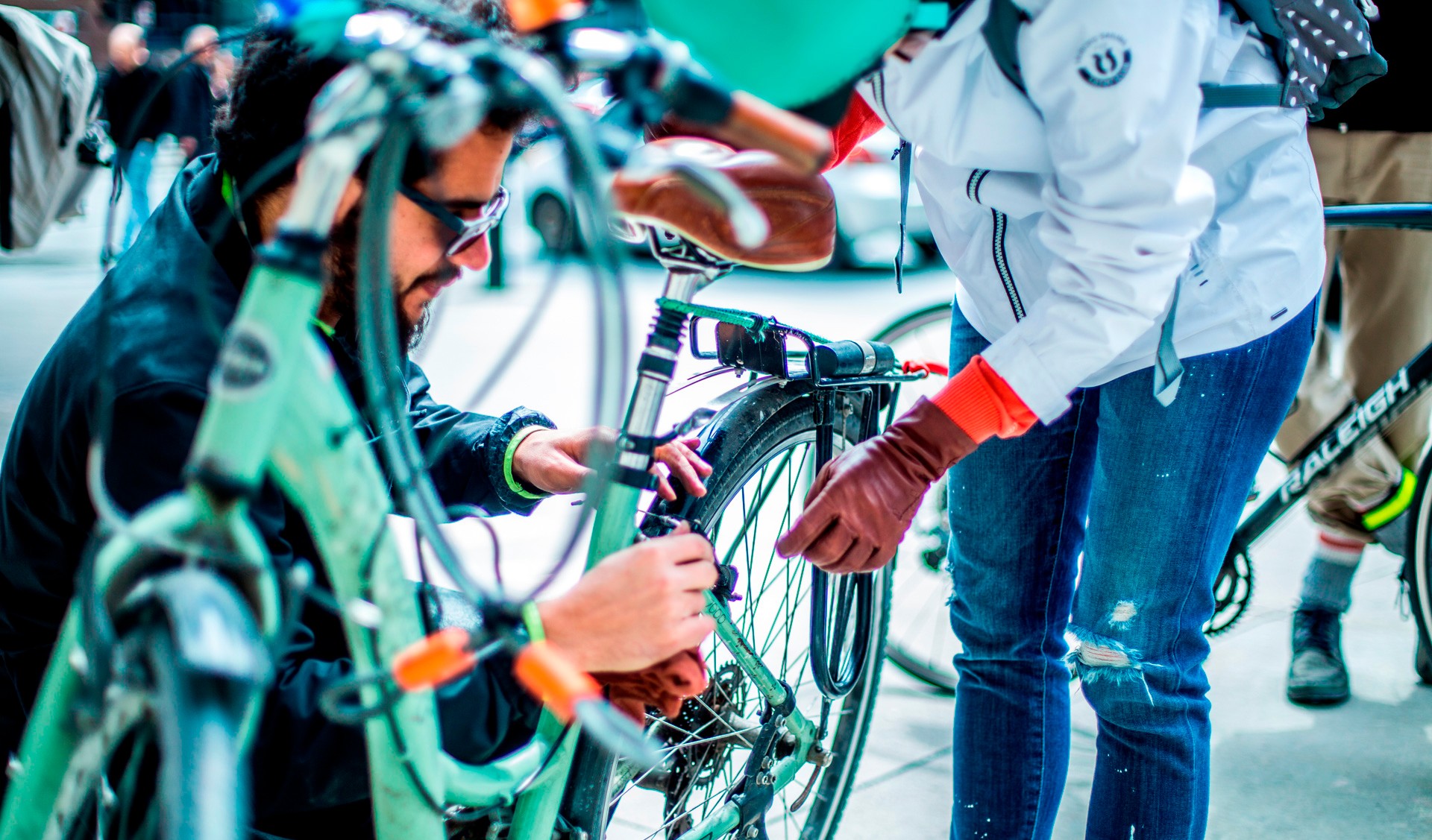 A man shows a cyclist wearing a helmet how to repair repairs their turqoise bike