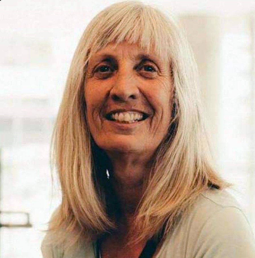 Andra McCartney, caucasian woman with white, shoulder length hair and bangs smiles at the camera.