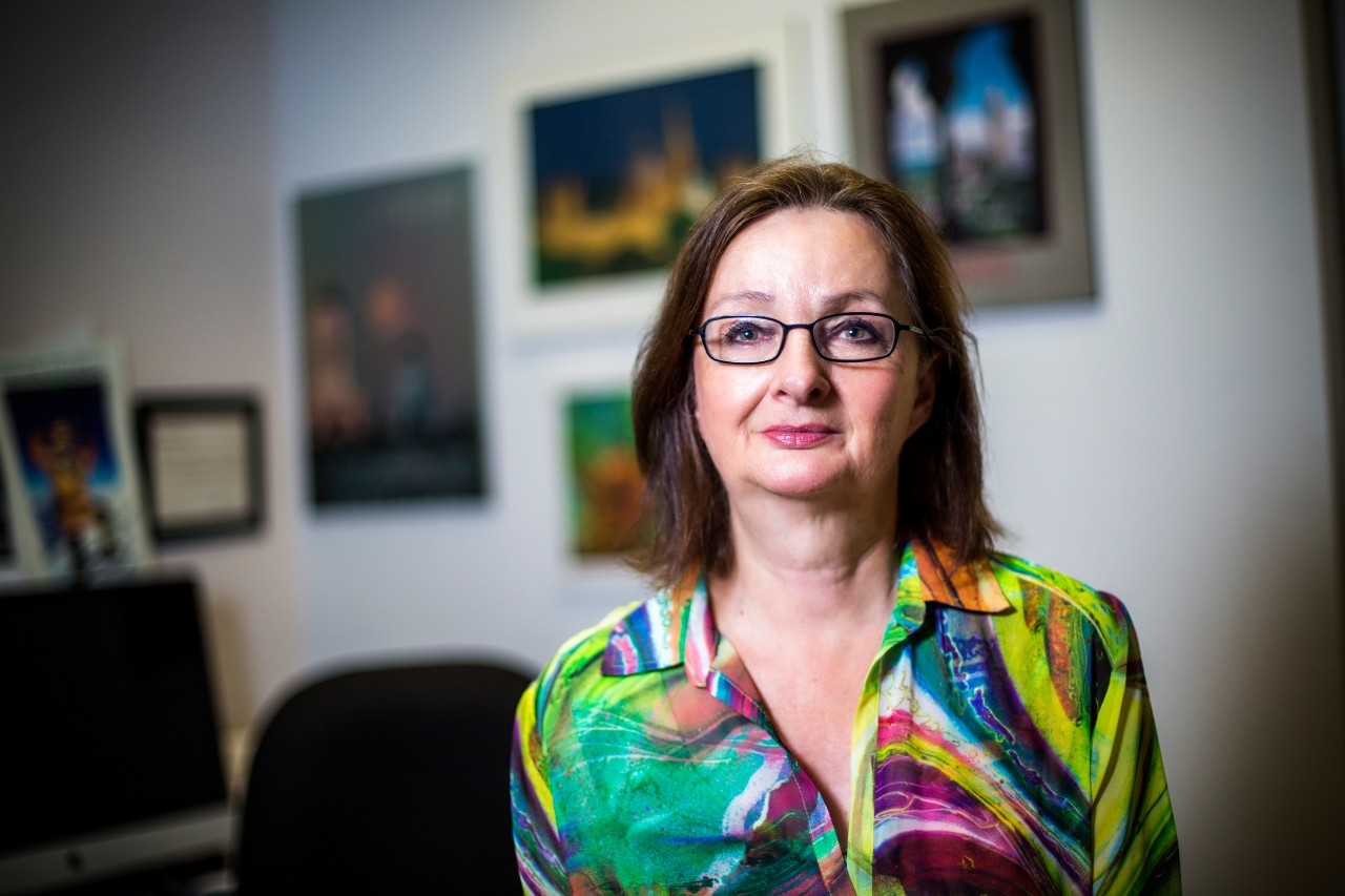 Diane Poulin-Dubois is pictured in her office. She has shoulder length brown hair, black rectangular framed glasses and a multicolored button-down shirt.