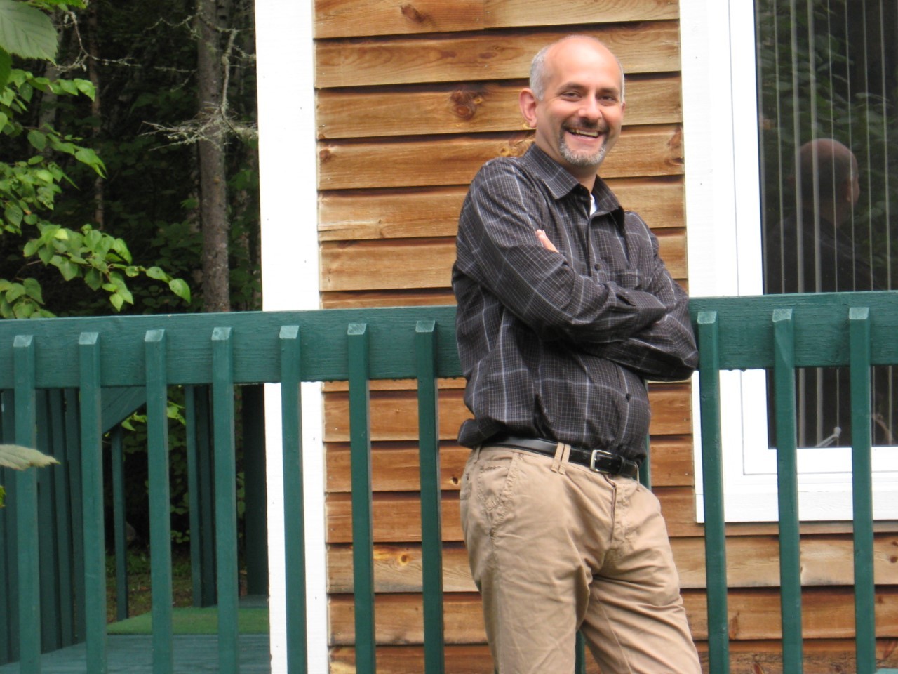 Aziz Choudry leans against a fence with arms crossed. He's smiling and has close-cropped salt and pepper hair and a goatee.