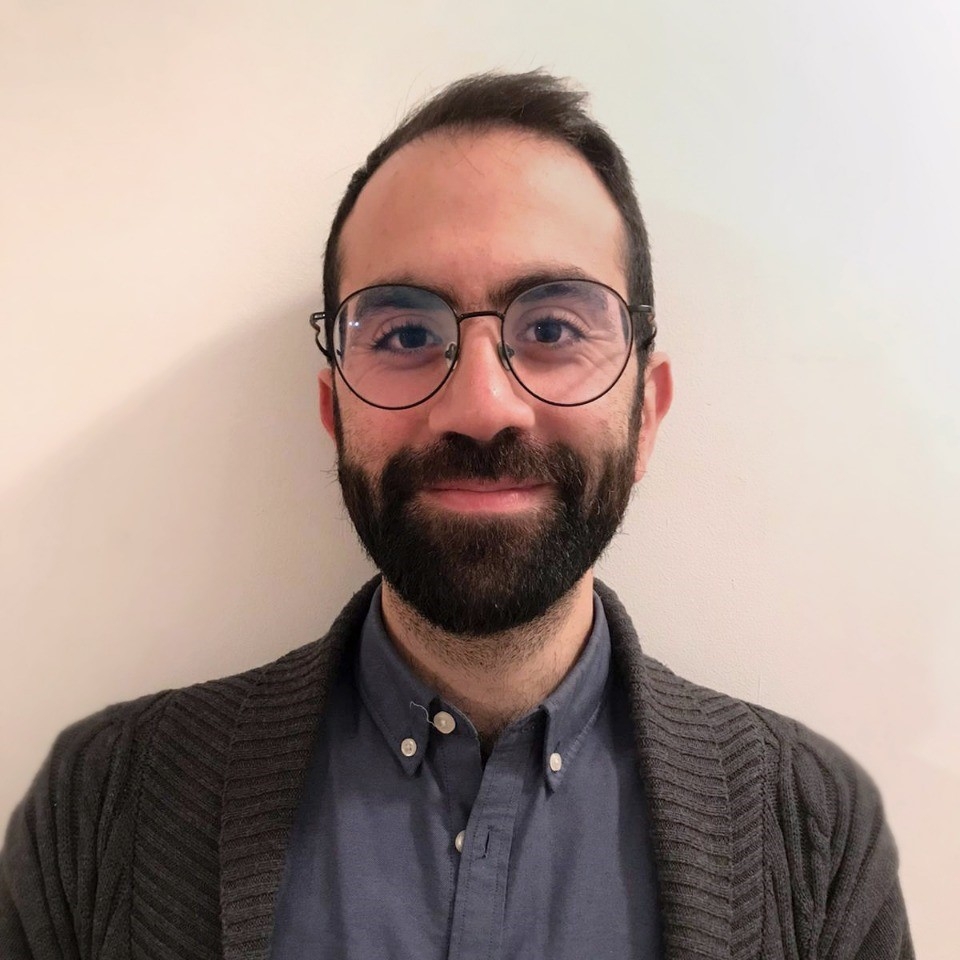 A portrait of a smiling man wearing a shirt, a cardigan and glasses