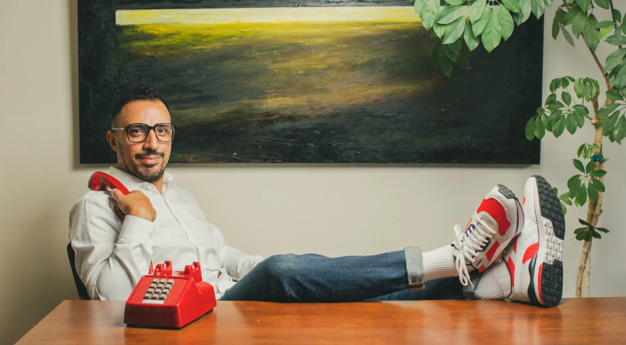 Dimitri Nasrallah sitting at a wooden desk with his feet up, and a red rotary phone