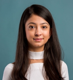 A smiling young woman with dark hair, wearing a white top, on a blue background