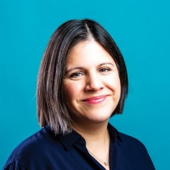 A smiling woman, with mid-length brown hair, wearing a dark top, on a turquoise background