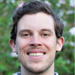 A smiling man with short brown hair, with trees in the background