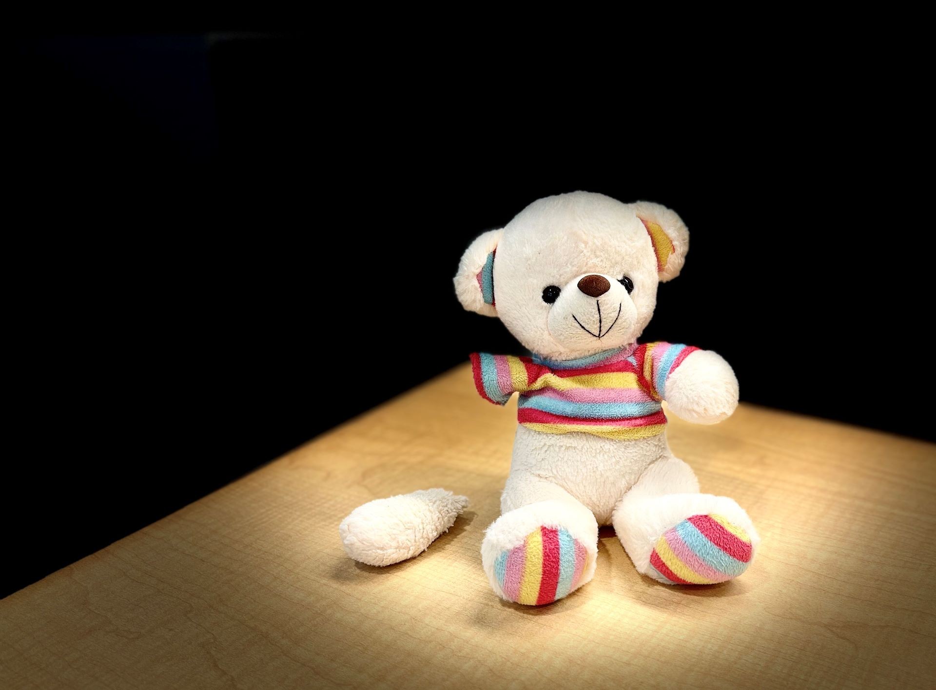 In this image, a small teddy bear sits with a broken arm. 