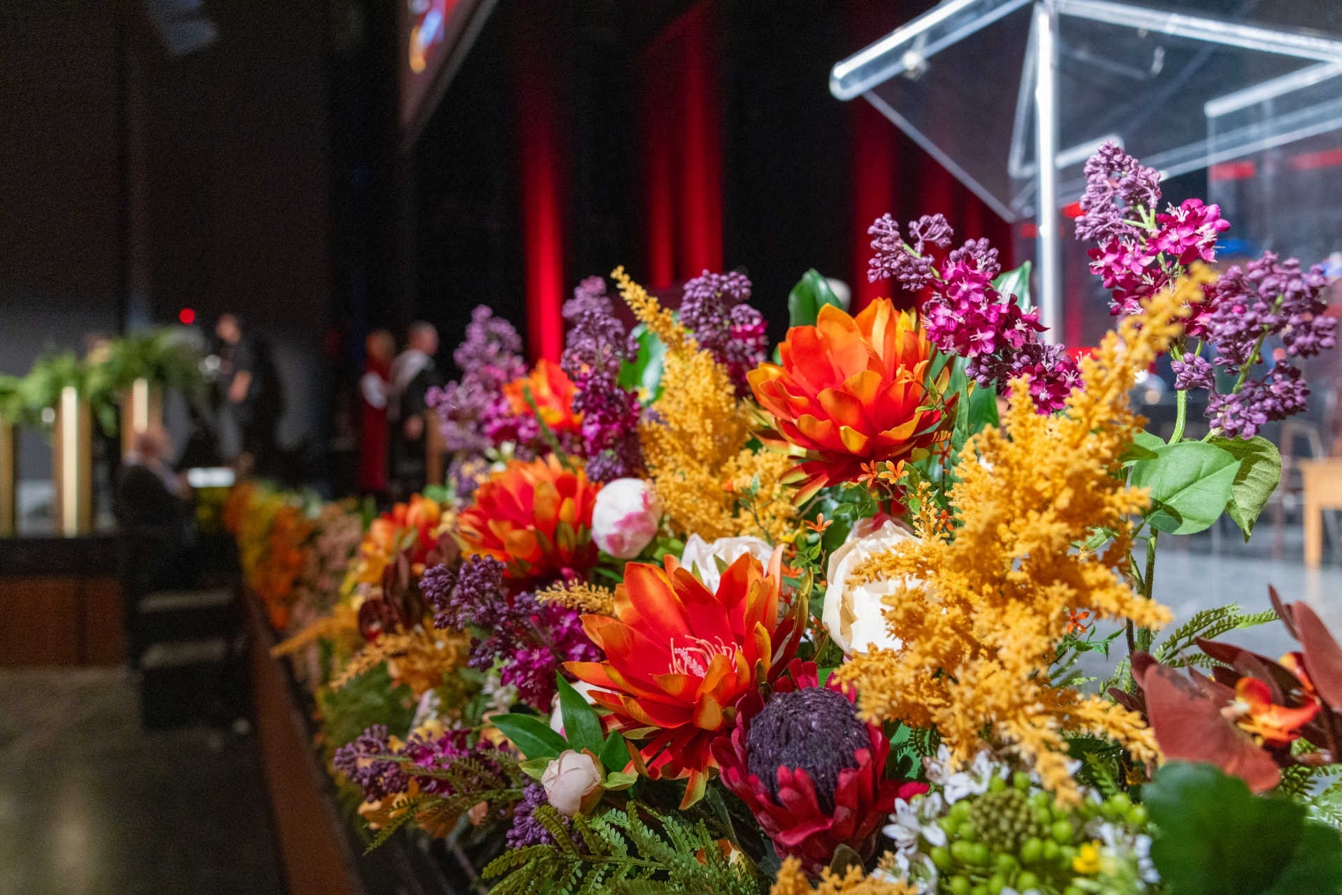 Colourful flowers set on a stage, seen from up close, with a transparent podium in the background