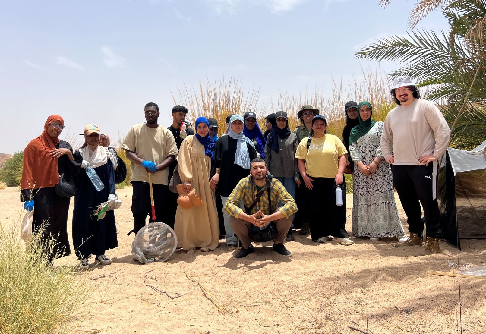 A multicultural group of a dozen students, in a desertic landscape, with prof Rassim Khelifa in the middle