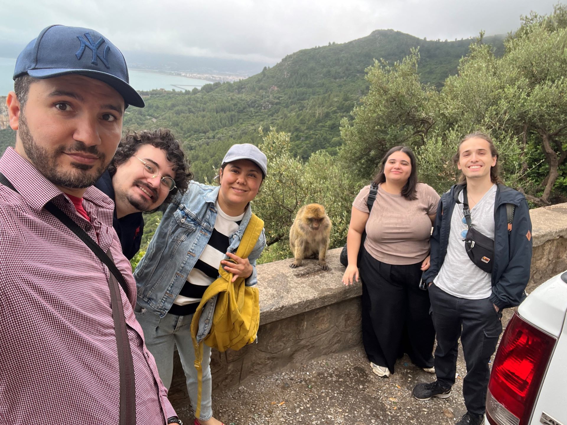 Four students and their teacher surrounding a medium size macaque, on the side of the road