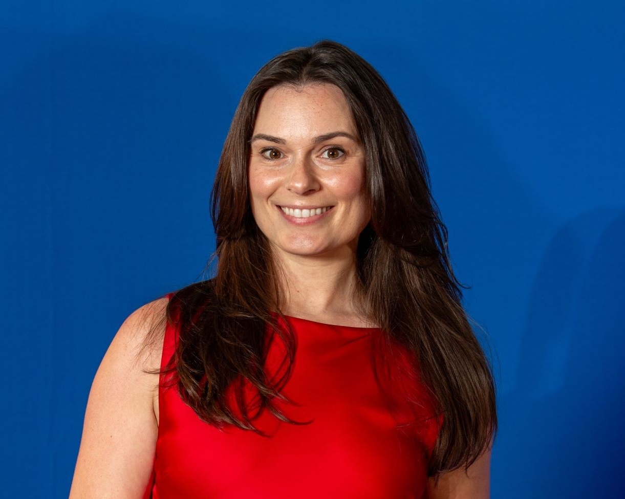 A smiling young woman with long brown hair, wearing a red dress, over a blue background