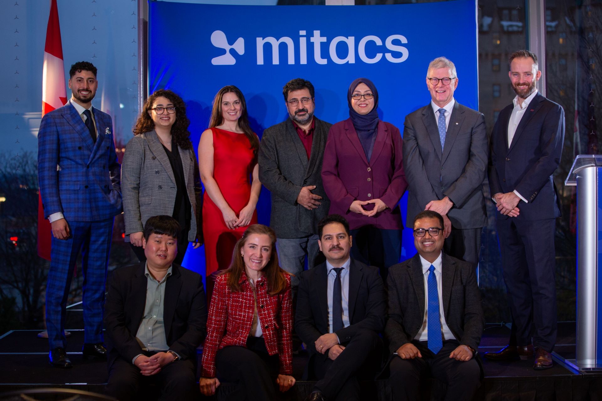 A dozen of smiling individuals posing at the award ceremony, on a blue background.