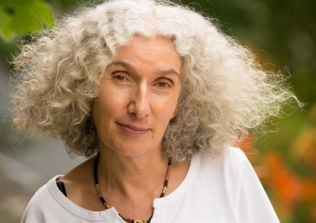 Cécile Rousseau smiles at the camera (white woman with curly white hair wearing a white top)