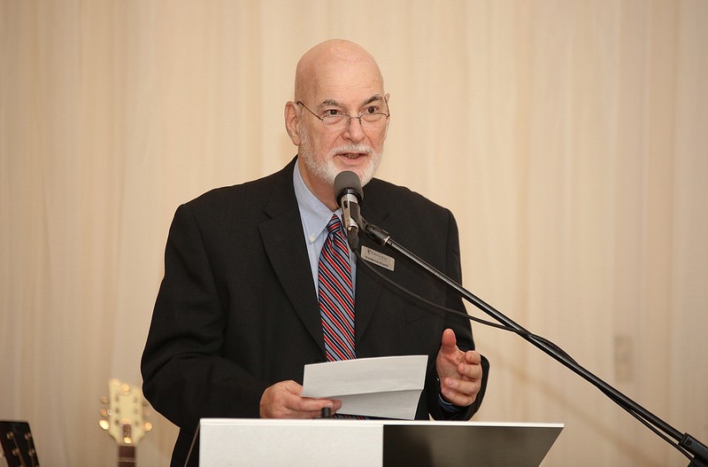Frederick Krantz wearing a suit and addressing a room with a microphone