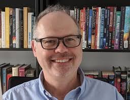 Headshot of a smiling André Gagné before filled book shelves