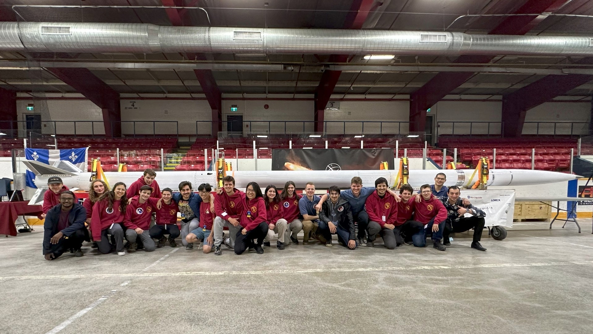 Members of Space Concordia Rocketry team kneel in front of their rocket.