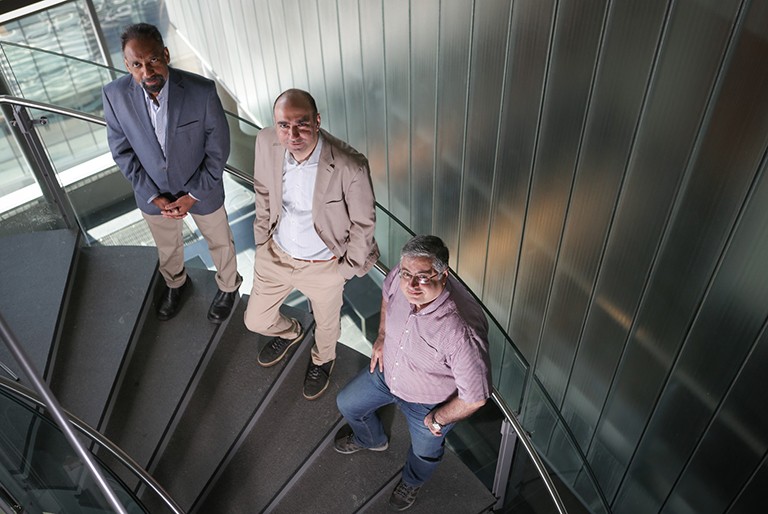 Three researchers stand on a flight of stairs looking up towards the camera