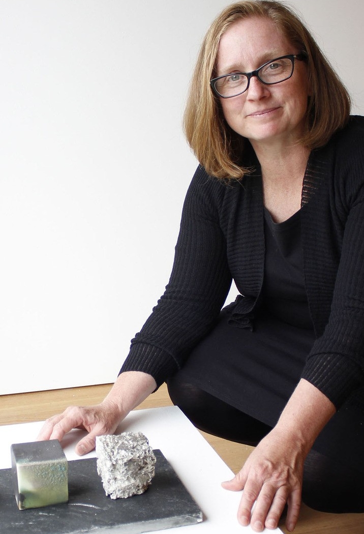 Woman with straight red hair with hands on table, paper and ceramics