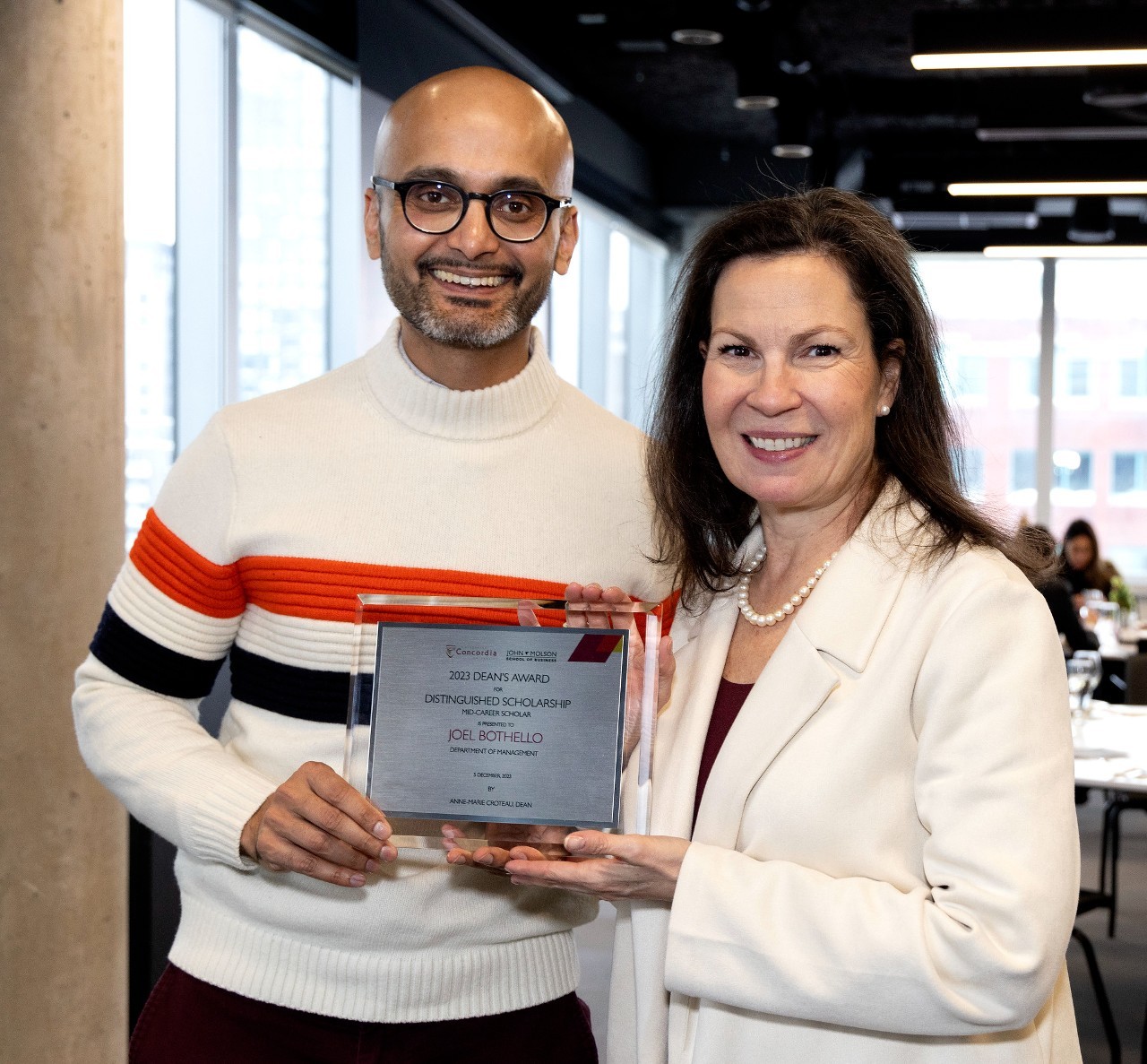 Joel Bothello accepts his award for Distinguished Scholarship: Mid-Career Scholar alongside Dean Anne-Marie Croteau
