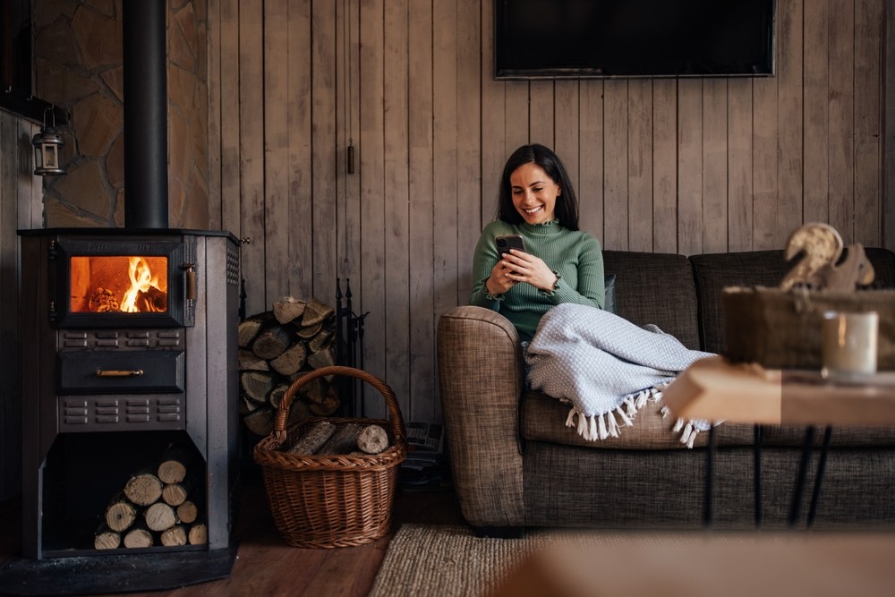 A woman sits by the fireplace and smiles at her cell phone