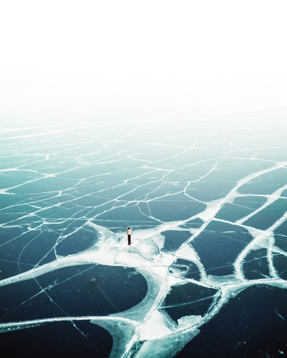 Aerial view of body of water covered in ice. Cracks in the ice are visible.