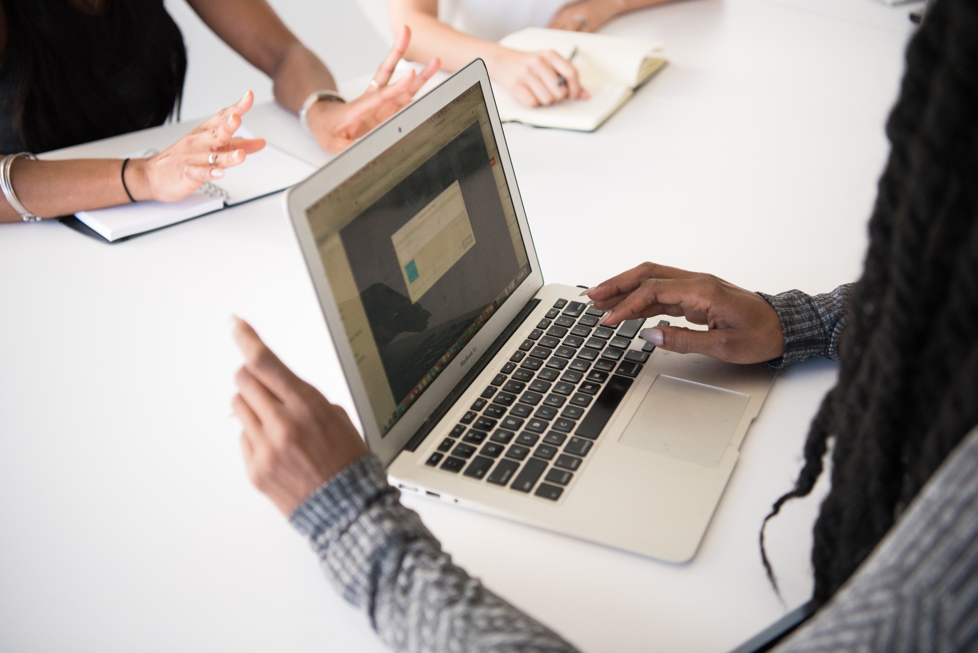 Three people around a white table having a meeting. Person in foreground has a laptop open