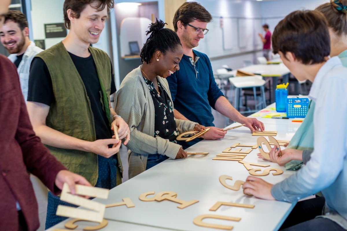 Group of people around a table playing with wooden letters as part of a residency at D3 Innovation Hub