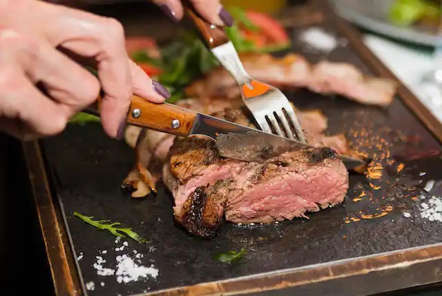 Close-up of hand cutting piece of meat with fork and knife