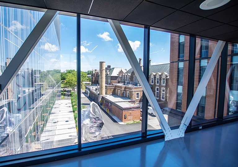 A corridor with glass windows looking out on a courtyard with a sculpture and brick buildings.