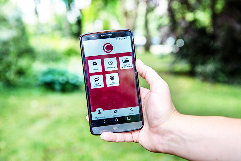 Hand holding an android phone with different graphics on the screen, and trees in the background.