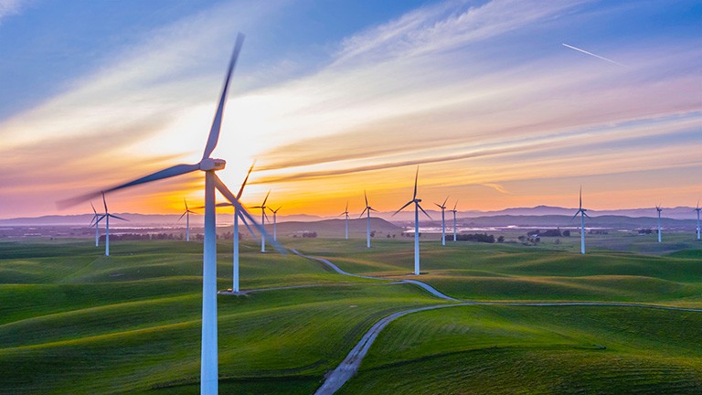 Sunset with rolling green hills and a windmill farm stretching into the distance.