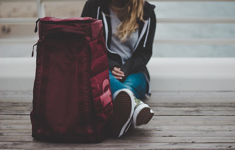 Young woman sitting on wooden deck, with a backpack in the foreground.