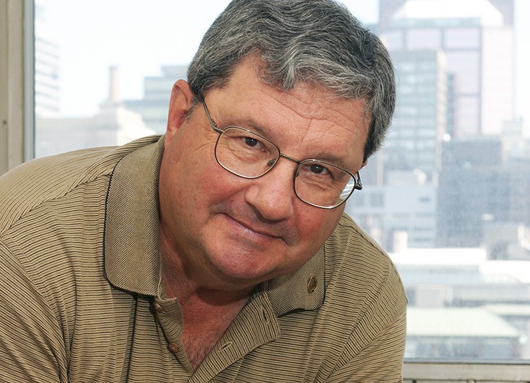 Older man with grey hair and glasses, in a tan polo shirt.