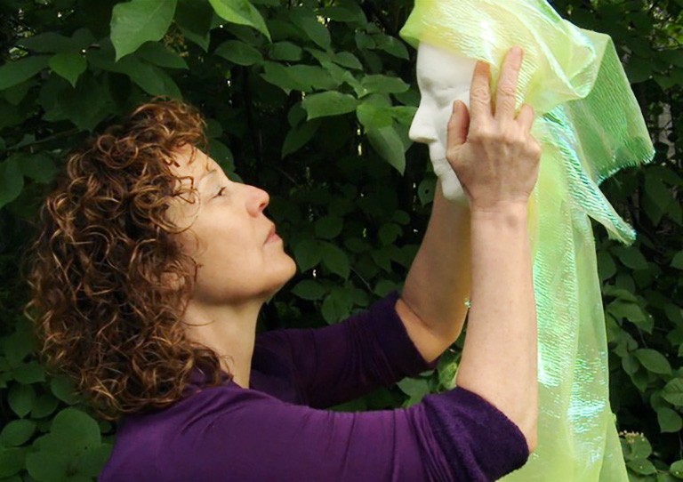 Woman with curly hair holding a mask in front of her and staring into its face.