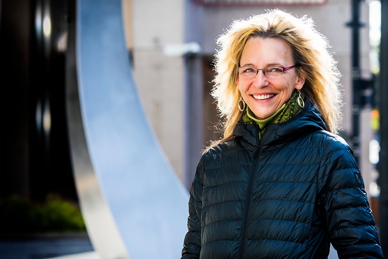 Portrait of smiling woman wearing glasses, dangling earrings and warm coat.