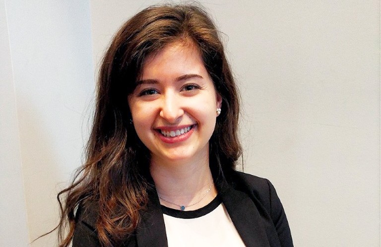 Smiling young woman with long dark hair, in a white shirt and black jacket.