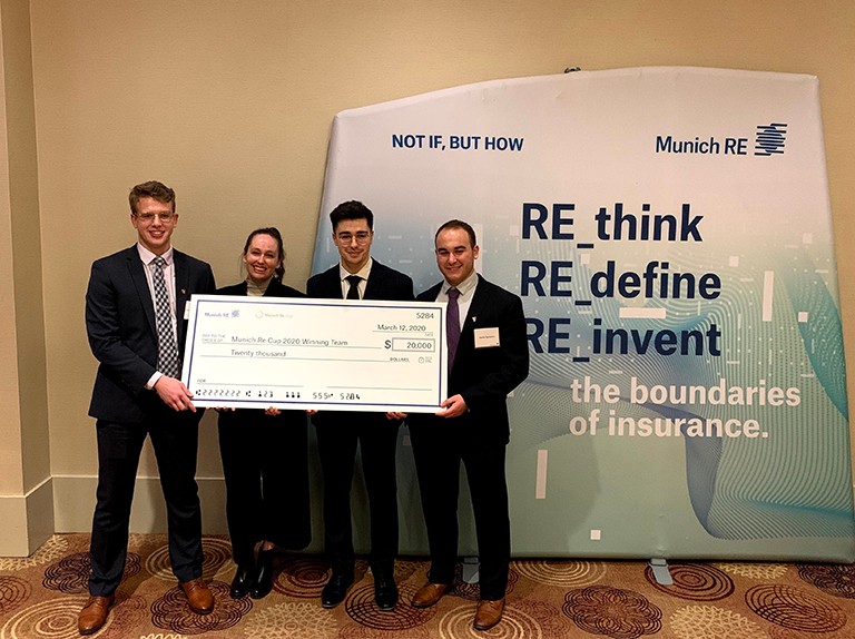 The Concordia actuarial mathematics team that won the prestigious Munich Re Cup in 2020: Jacob Blair, Catherine Dagenais-Roberge, Ioannis Volakakis and Daniel Sylvestre. Four Concordia students in formal attire holding a big cheque in front of a Munich RE banner.