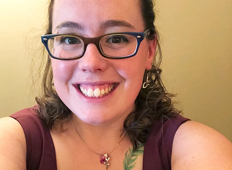 Young smiling woman with long dark hair and glasses.